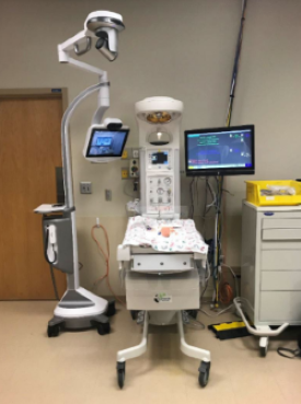 Large medical device with an area to place a baby and a camera above.