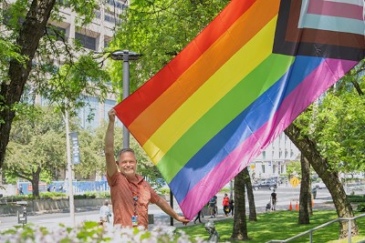 A person holding a large Pride flag by the University entrance of the hospital.
