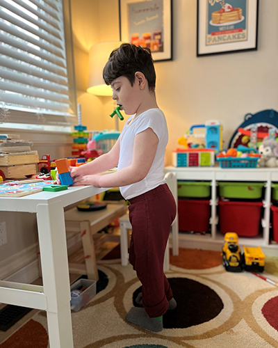 Child stands at table playing with blocks. 