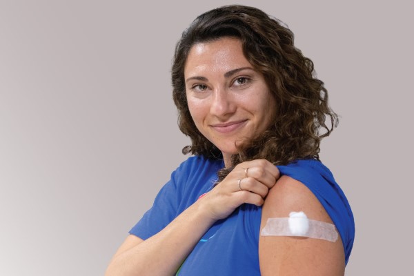 A woman lifts her t-shirt sleeve to show a bandage covering her flu shot injection. 