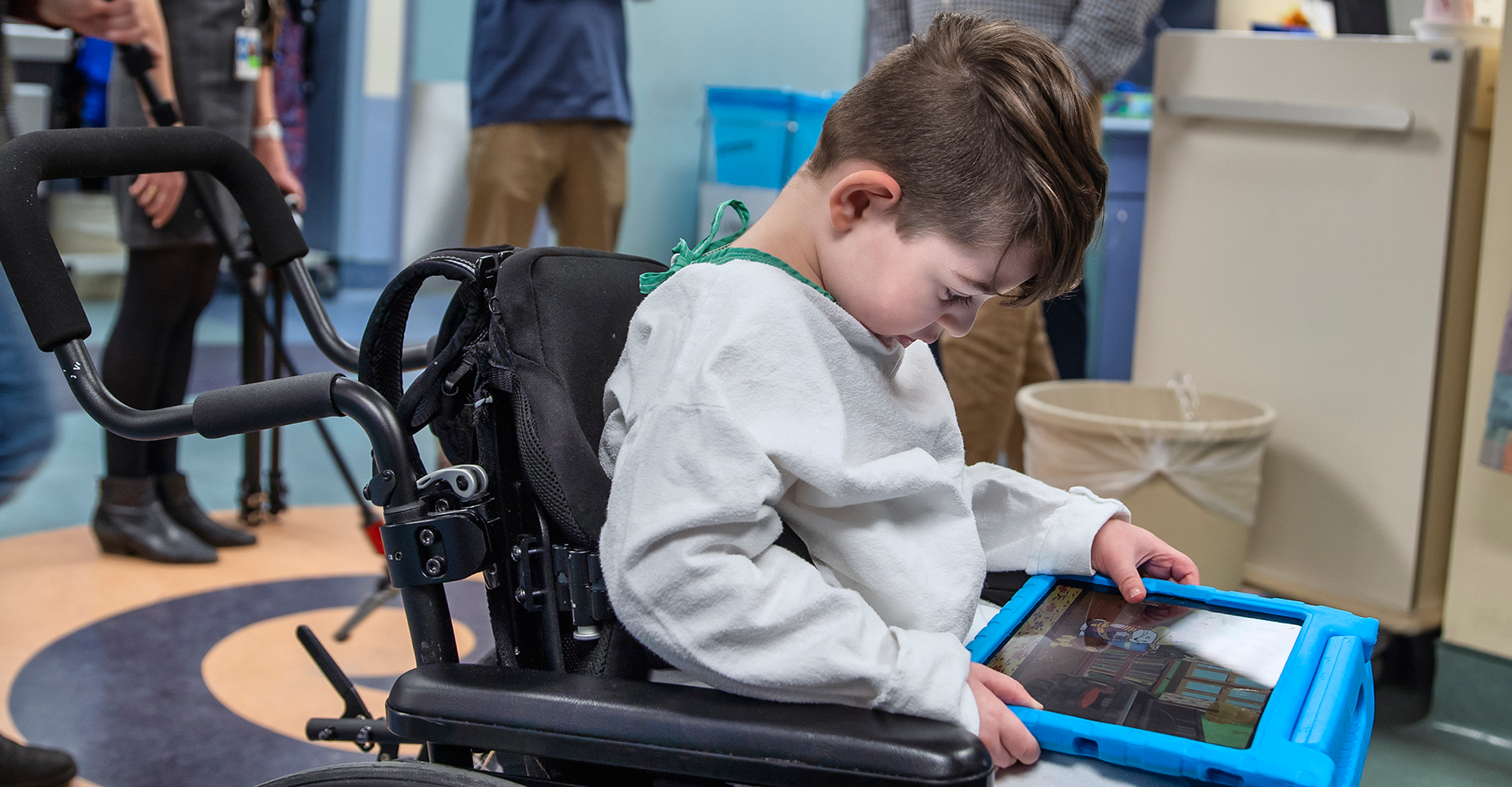 Child sits in wheelchair playing with tablet. 