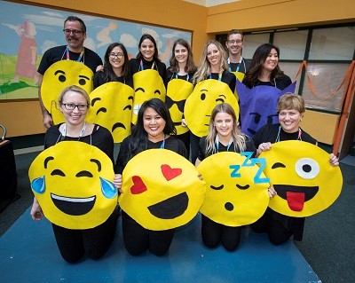 Large group of adults wearing costumes that look like face emoticons/emojis.