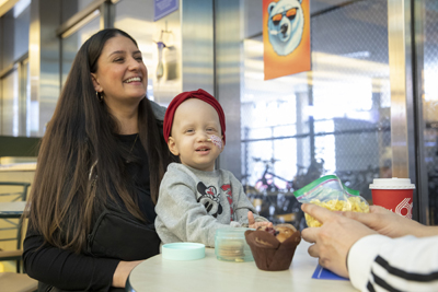 A child with a feeding tube attached seated on their parent's lab at a table