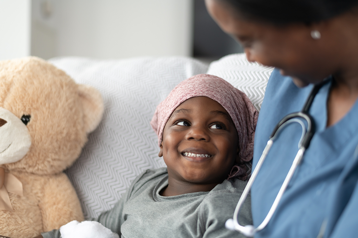 A young girl sits on a hospital bed smiling at her physician.