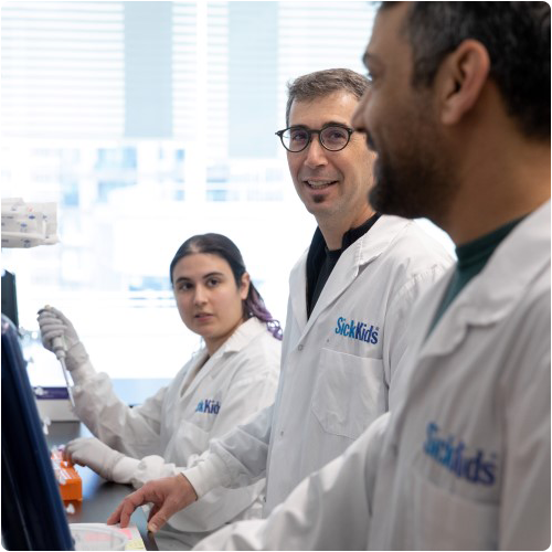 Adam Shlien and team members in SickKids branded lab coats standing at a lab bench and conversing.