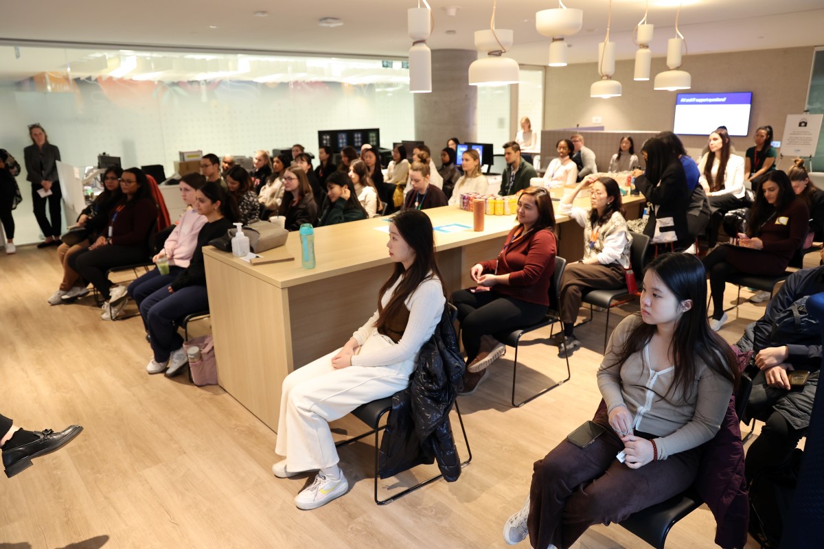 Group seated in a bright room with wooden floors, listening to a presentation.