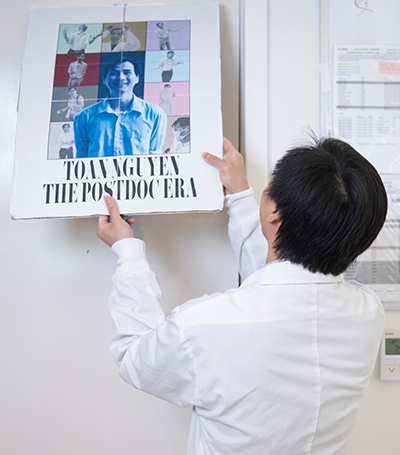 Dr. Toan Nguyen puts up a poster with a photo of himself with the words "The postdoc era". 