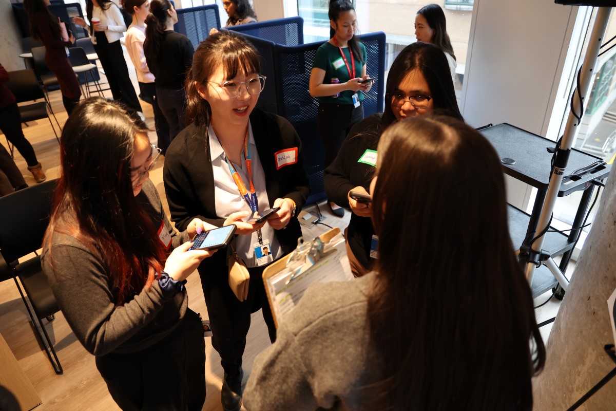 Group of people wearing name tags and lanyards, standing in a circle and chatting at a professional event.