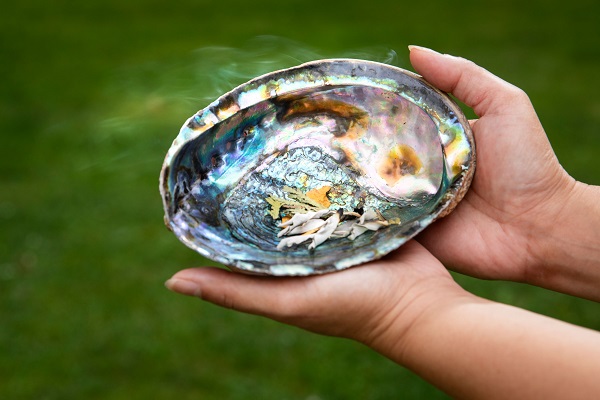 Hands holding an abalone shell for smudging.