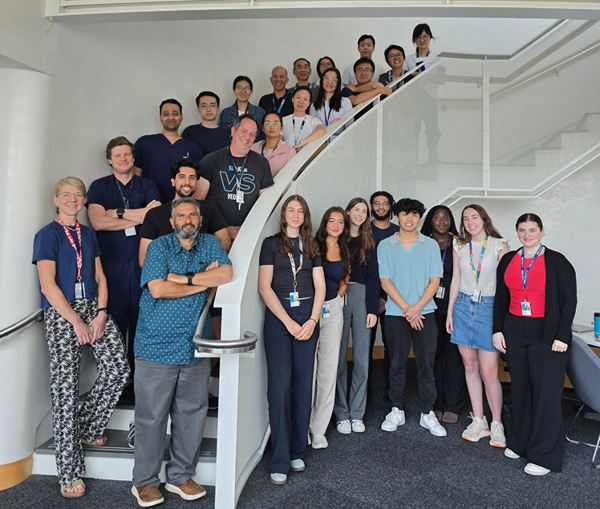 A large group of members from the Aleixo Muise lab stand in the Peter Gilgan Centre for Research and Learning smiling at the camera