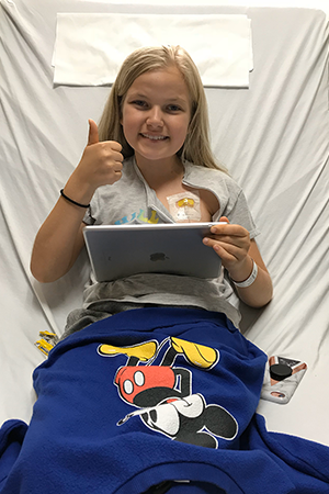 A young girl lays in a hospital bed, smiling at the camera.