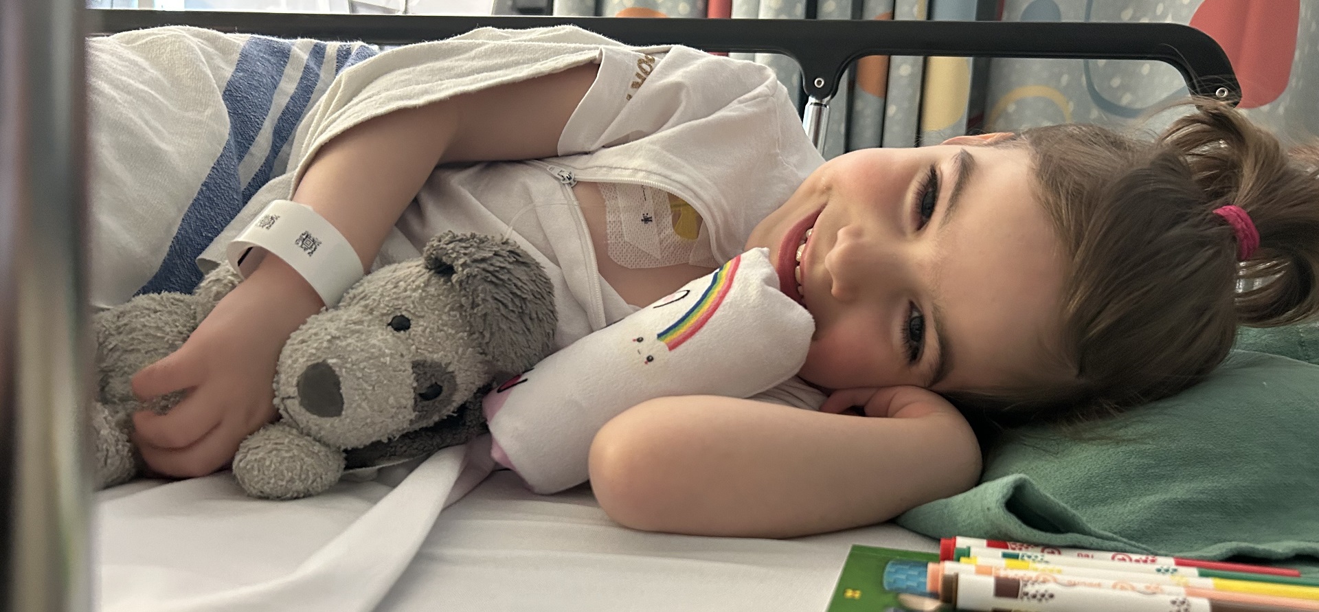 A child lays on their side in a hospital bed holding a stuffed toy.