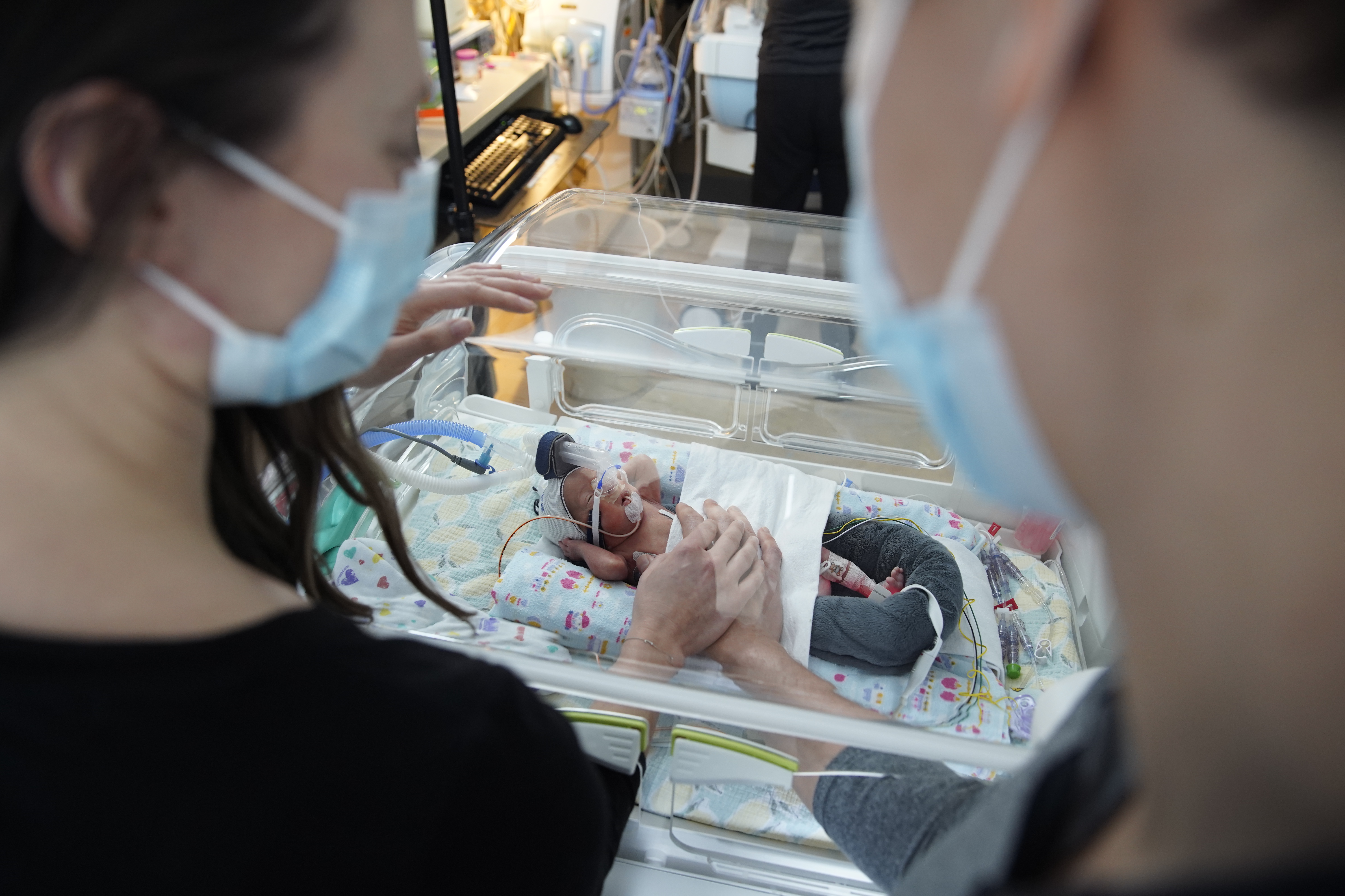 Erica and Brett in the SickKids NICU standing with Jeff in an incubator. 