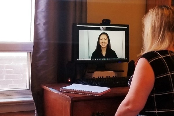 A woman sits in front of a computer and speaks with another woman via video conferencing.