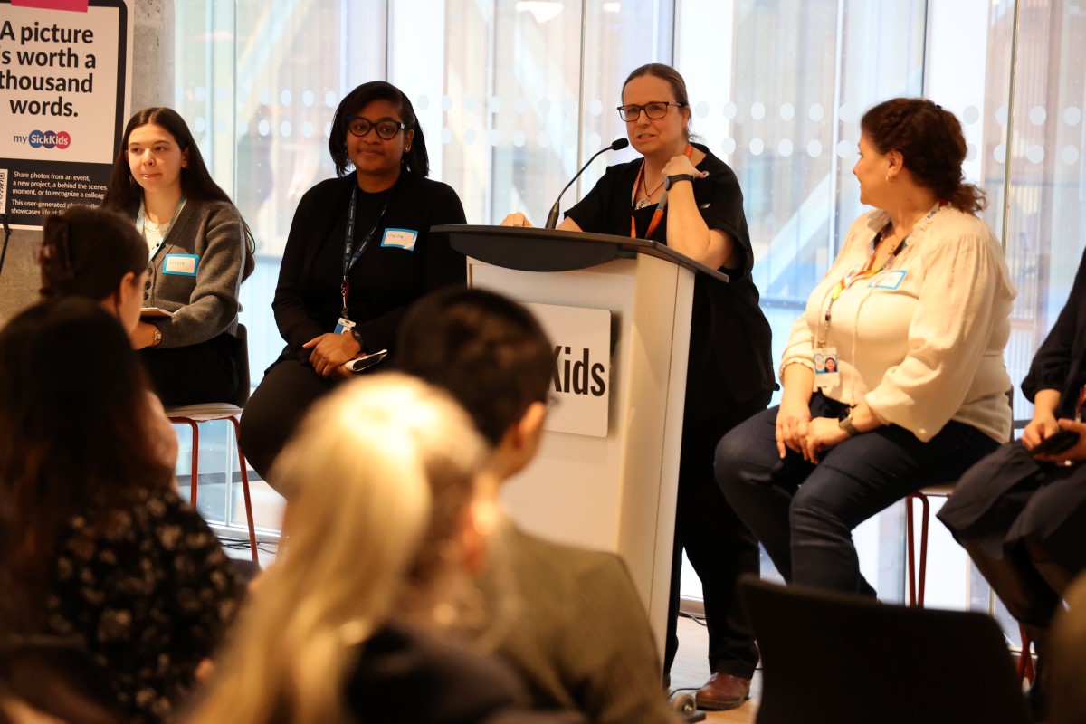 Four panelists seated on stools with one speaking at a podium ; sign behind reads 'A picture is worth a thousand words.'