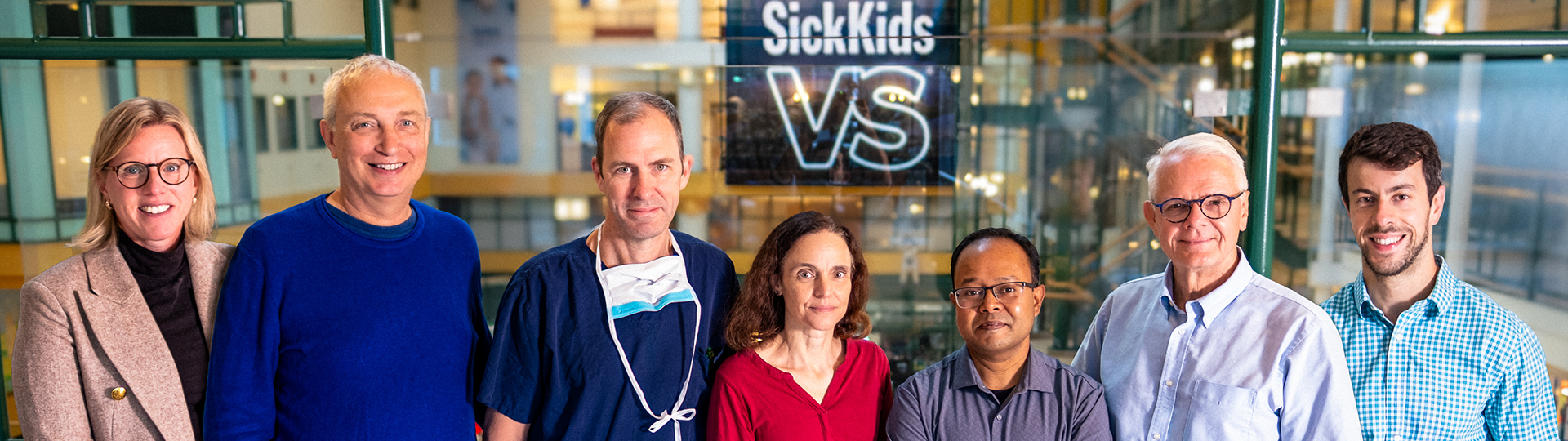 Seven scientists and clinicians smiling in SickKids hospital.