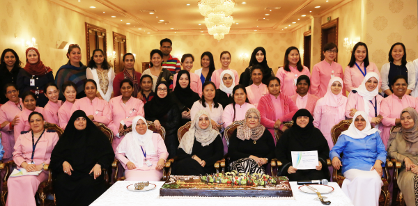 Group of healthcare professionals in Qatar-SickKids partnership wearing pink uniforms, gathered for celebration with ceremonial cake.