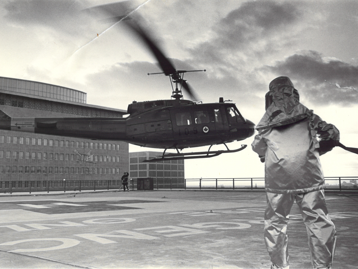 A black and white photograph showing a medical evacuation helicopter landing on a hospital rooftop helipad. 