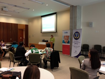 A SickKids Global presentation showing woman in green giving talk with hospital banners displaying "Center for Learning Excellence 2012."