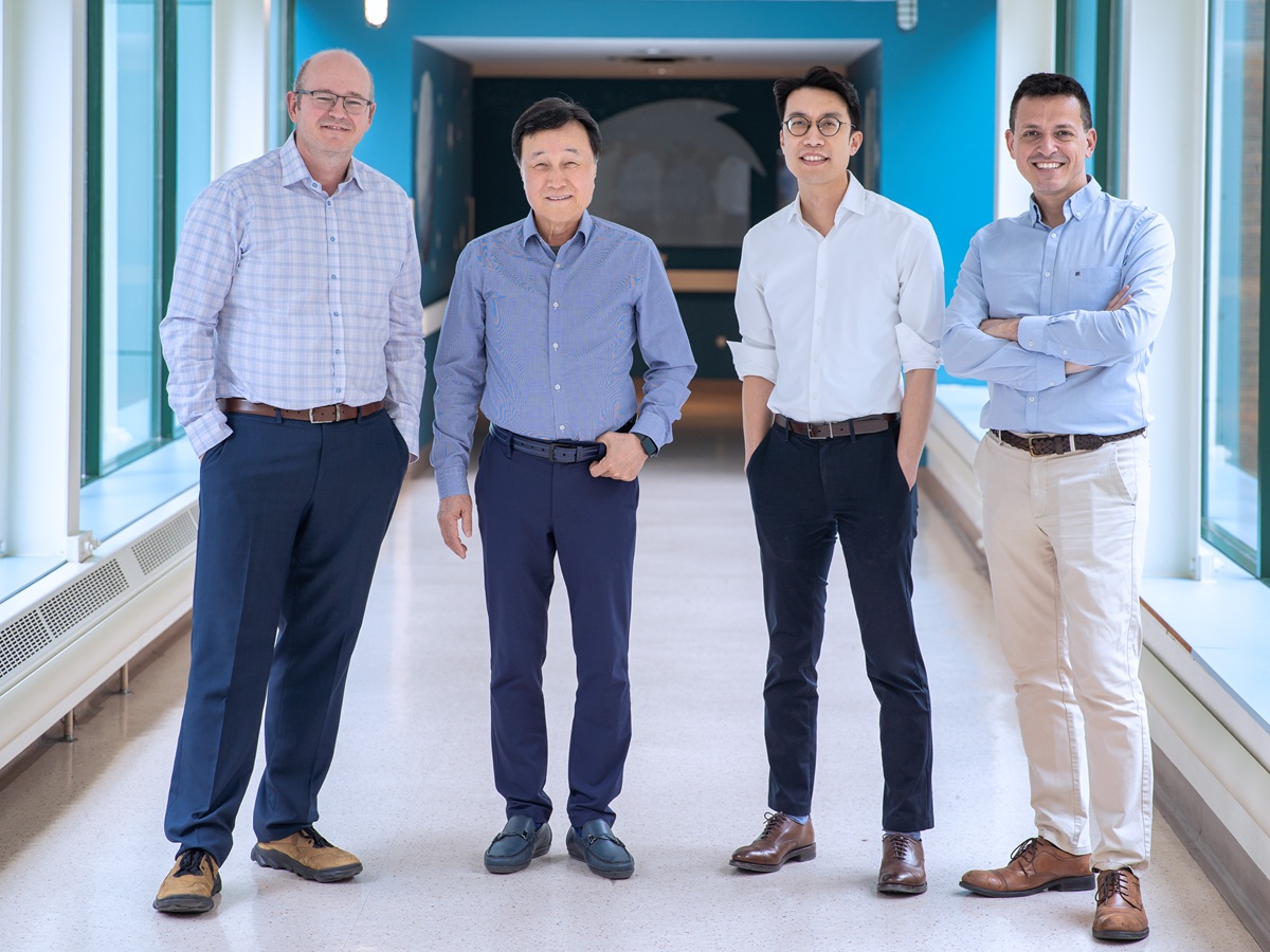 Four people standing in a bright hallway with large windows, wearing business casual clothing and dress shoes.
