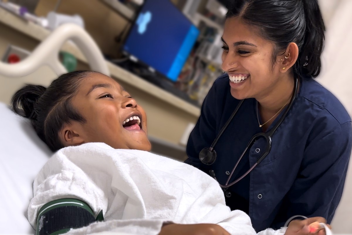 Health-care provider and child on a hospital bed smiling together.