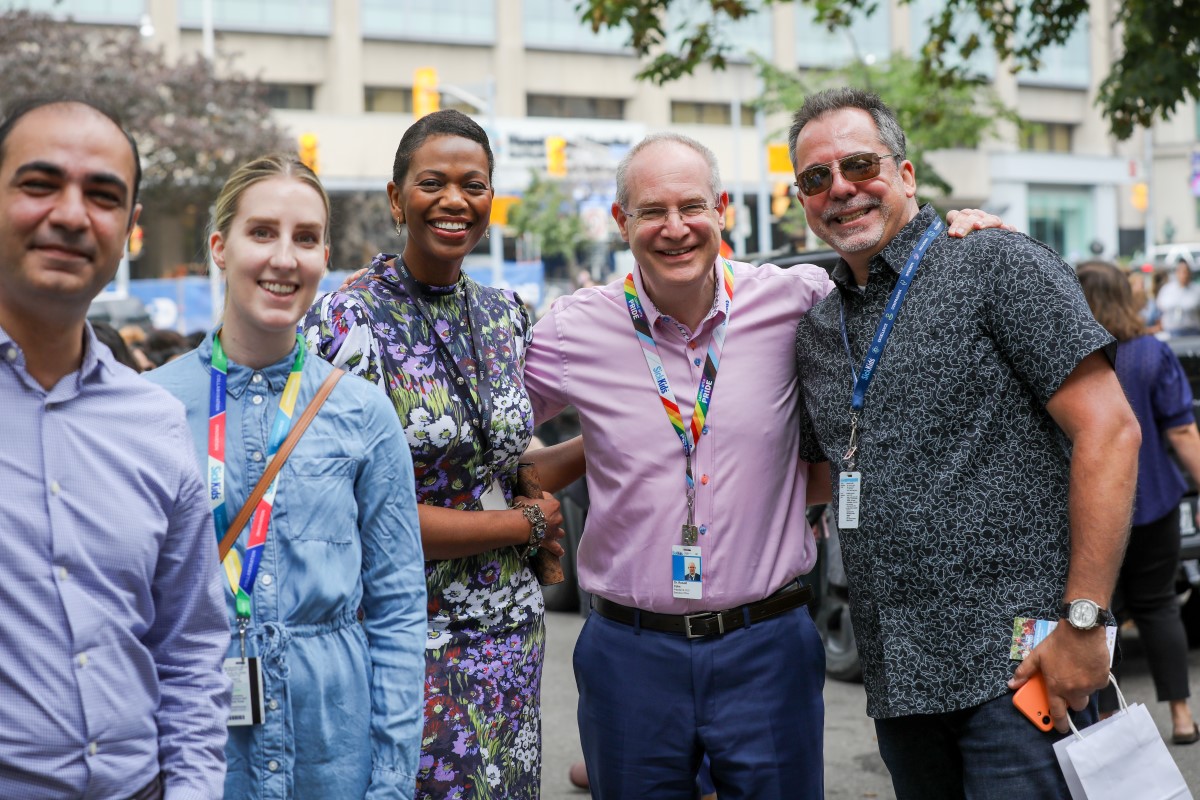 Five staff stand together smiling outdoors.