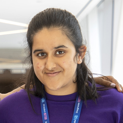 Headshot of young woman wearing a purple t-shirt and SickKids lanyard.
