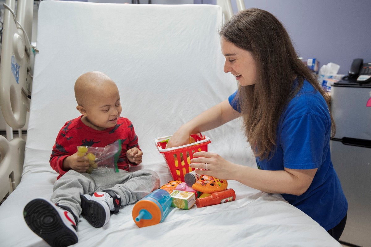 Young adult and child seated on a hospital bed playing with toy food.
