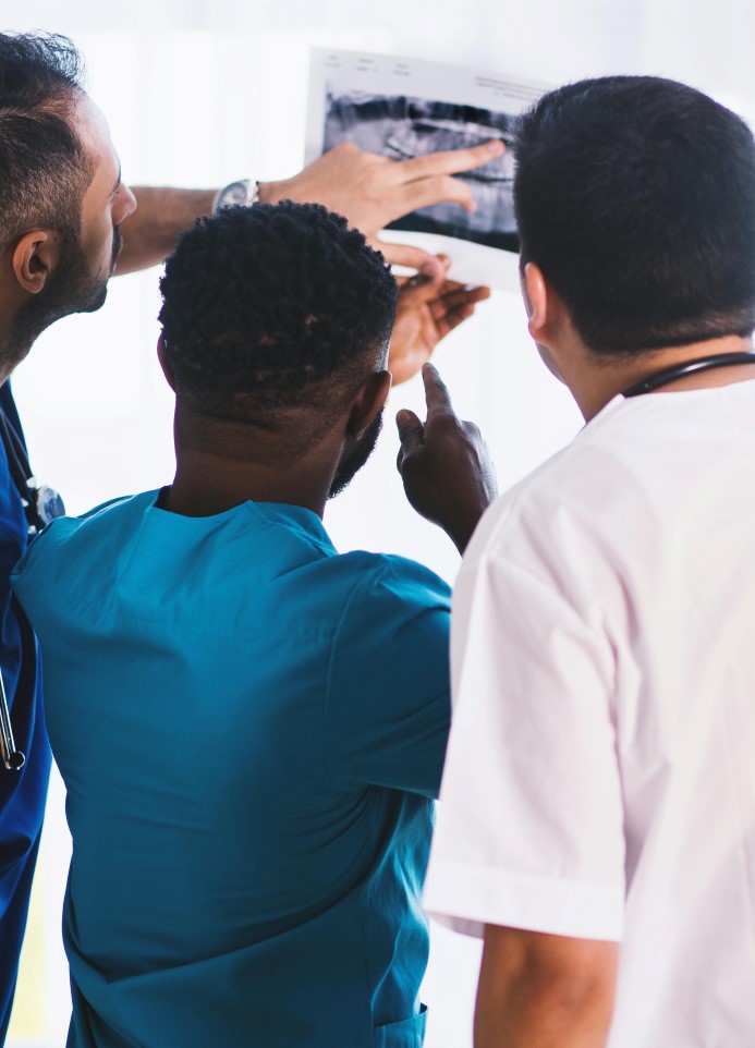 Three healthcare professionals in scrubs examining medical imaging or X-ray results together in a bright clinical setting.