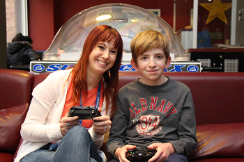 A woman and teen boy sit on a couch holding gaming controllers
