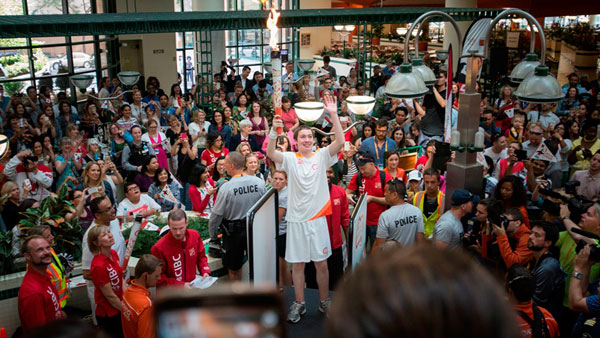 A boy holding the pan am torch stands on stage waving to crowds of people standing around him