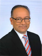 Headshot of man wearing a suit and tie, as well as glasses.