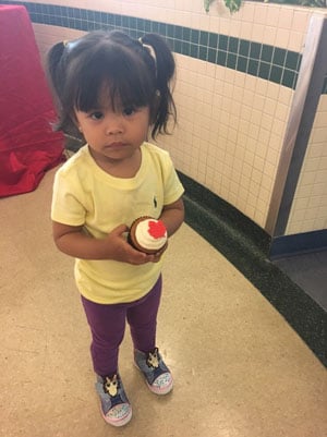 Toddler holds a cupcake with a maple leaf on it.