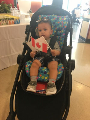 Baby in stroller holds Canada flag.