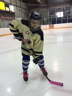 Girl in hockey gear leans on her stick, standing on an indoor rink.