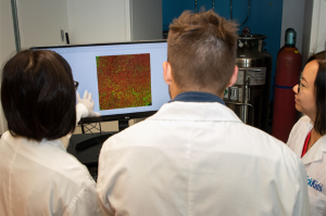Three people in lab coats looking at a computer screen with a square image on the screen.