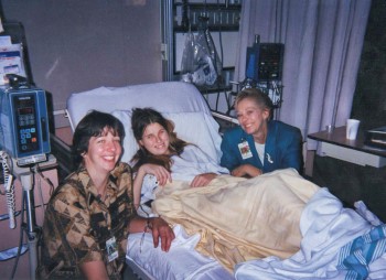 Kristina smiles from her hospital bed, while Rita and Moira smile at either side of the bed.