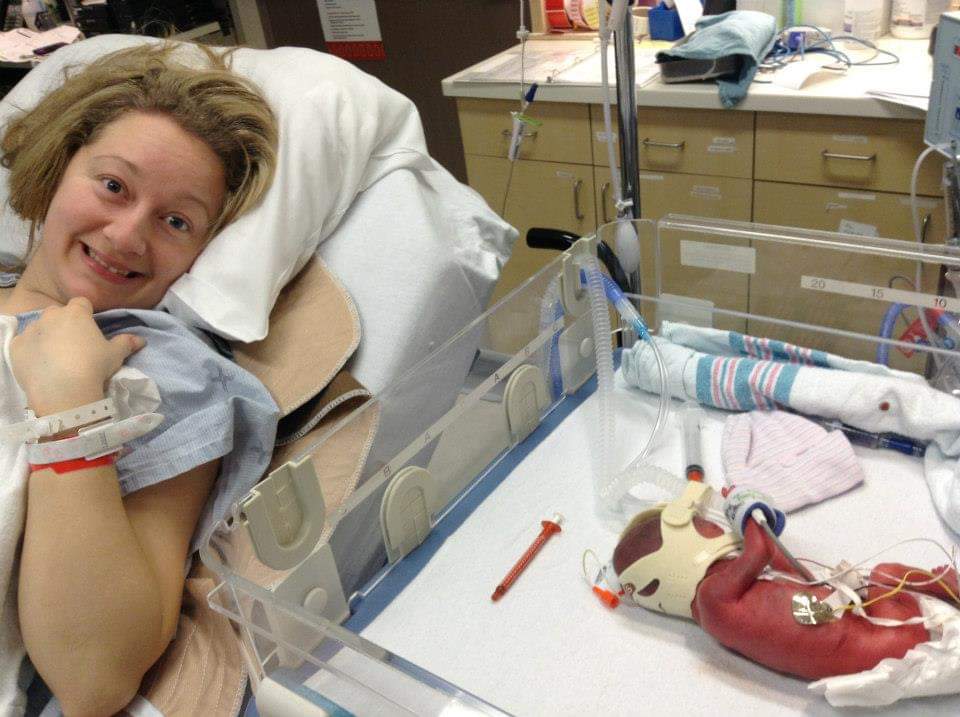 Jessica in a hospital bed pointing at Ben in his incubator. 