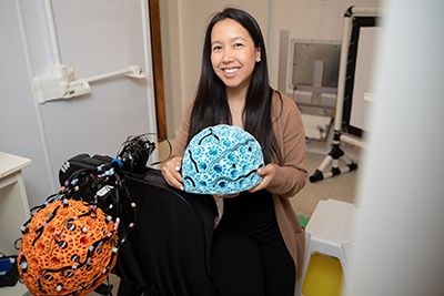 Dr. Julie Sato holding wearable brain scanners, which are shaped like helmets.