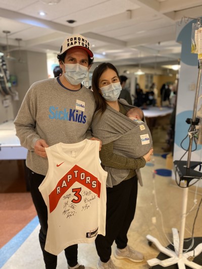 Taylor and Kori posing for a photo with Milo. Taylor is holding a signed Raptors jersey.