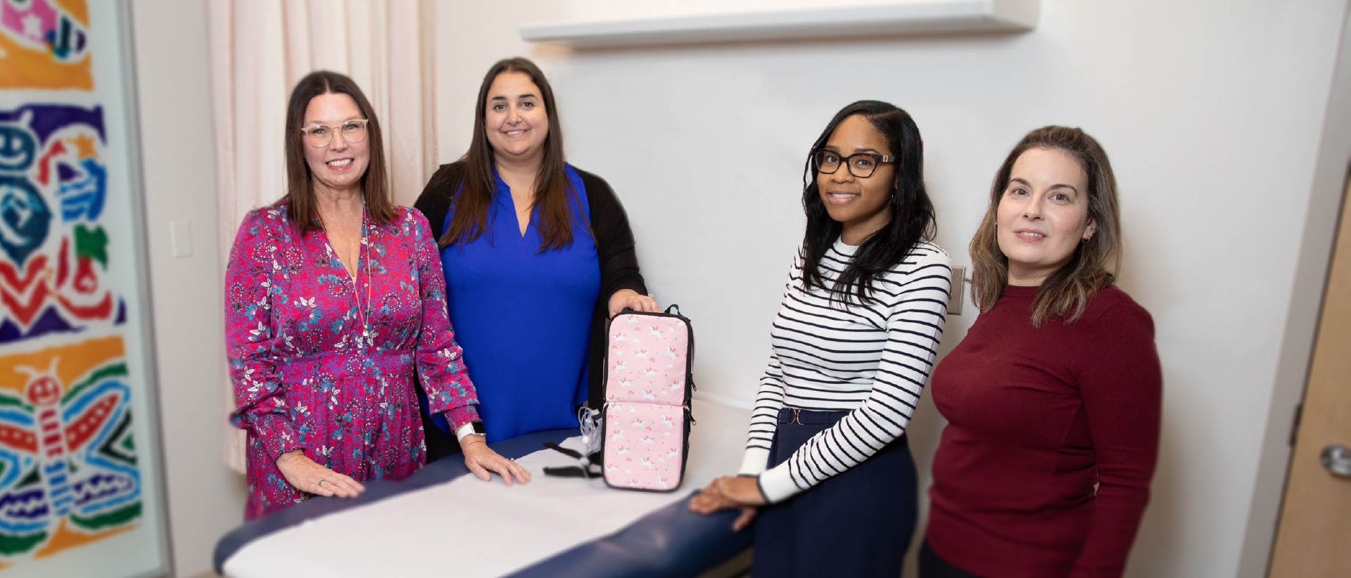 Sue Zapanec, Alia Petropoulos, Chantel Campbell and Lisa Honeyford posing for a team photo. Alia is holding up a pink Blina Backpack with a unicorn pattern.