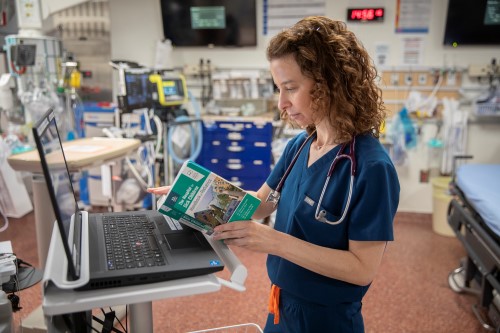 Dr. Deborah Schonfeld rests The Hospital for Sick Children Handbook of Paediatrics against a laptop on a stand in a trauma room in the emergency department.