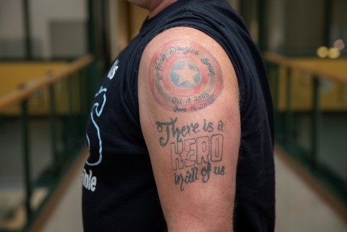 Doug's tattoo, a red and blue shield with a star in the middle along with Noah's name and the date he was born and the date he died. Text underneath reads "There is a HERO in all of us."