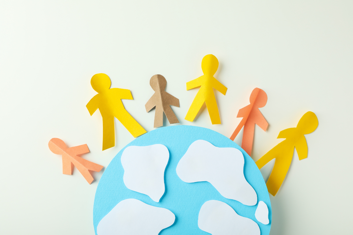 Paper cutouts of people figures standing on top of a paper cutout of the Earth.