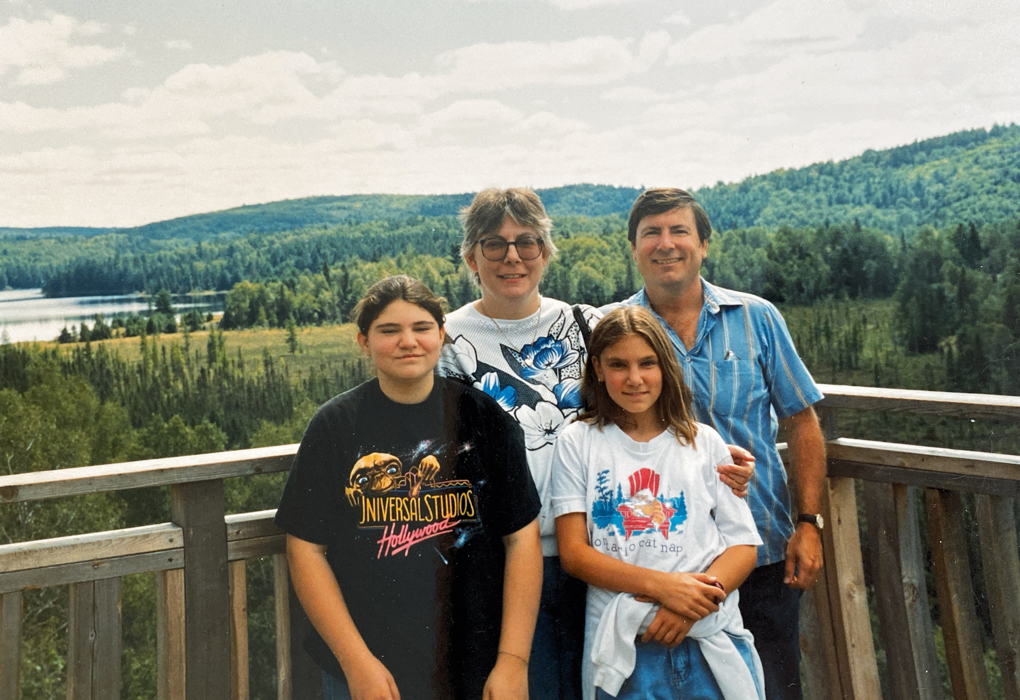Natalie standing with her sister, mom and dad, with a forest and water in the background.