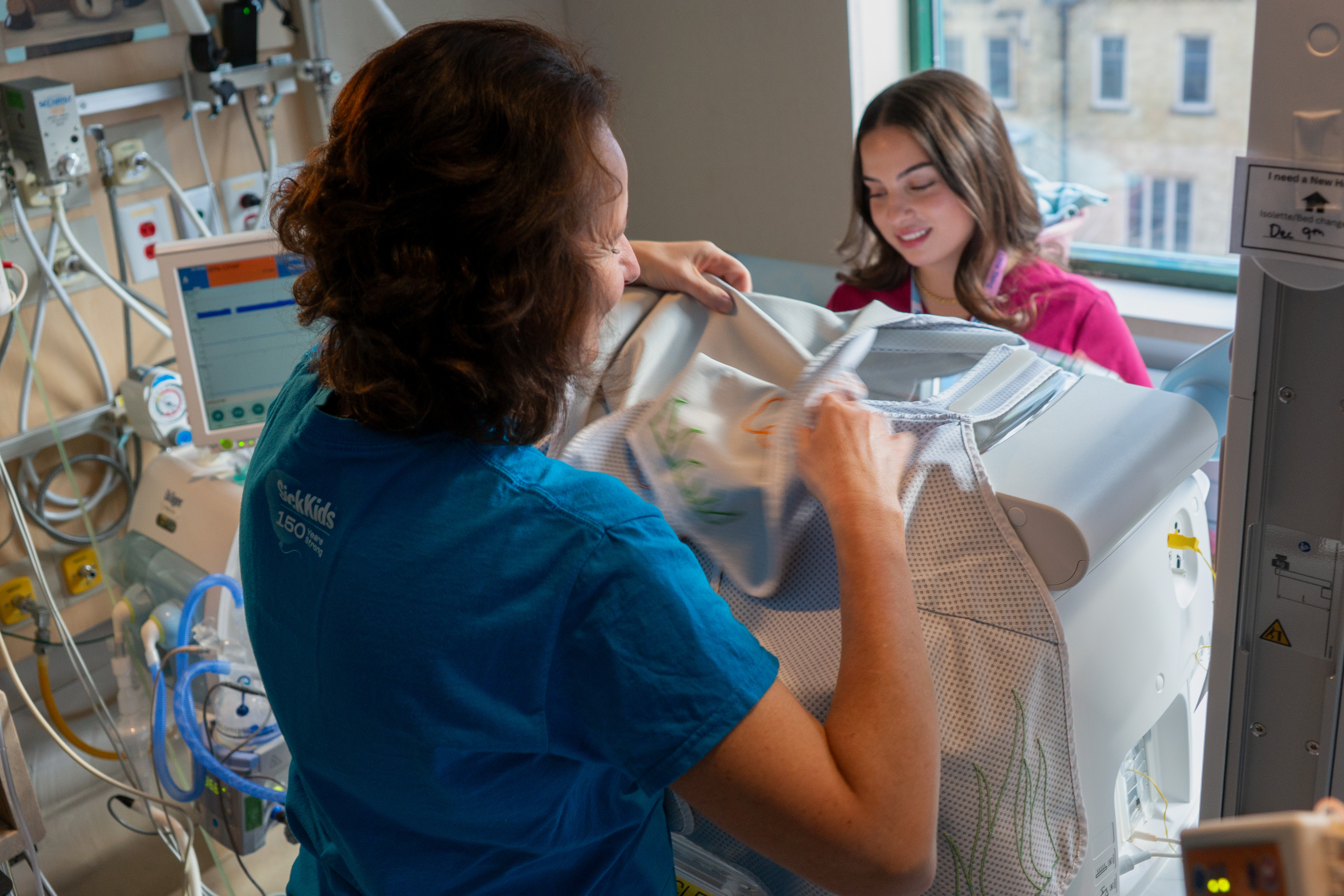 Franze and Yevel place a drape over an incubator in a NICU room.