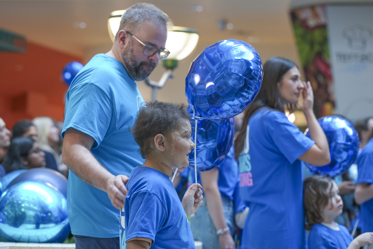 A father and child dressed in blue SickKids t-shirts. The child is holding a blue balloon.