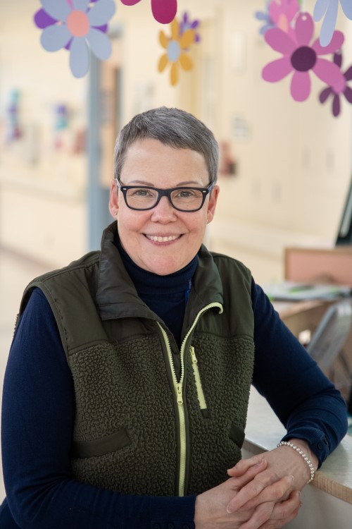 Jane Darch stands smiling in front of a clinic desk with flower decorations hanging above her head.
