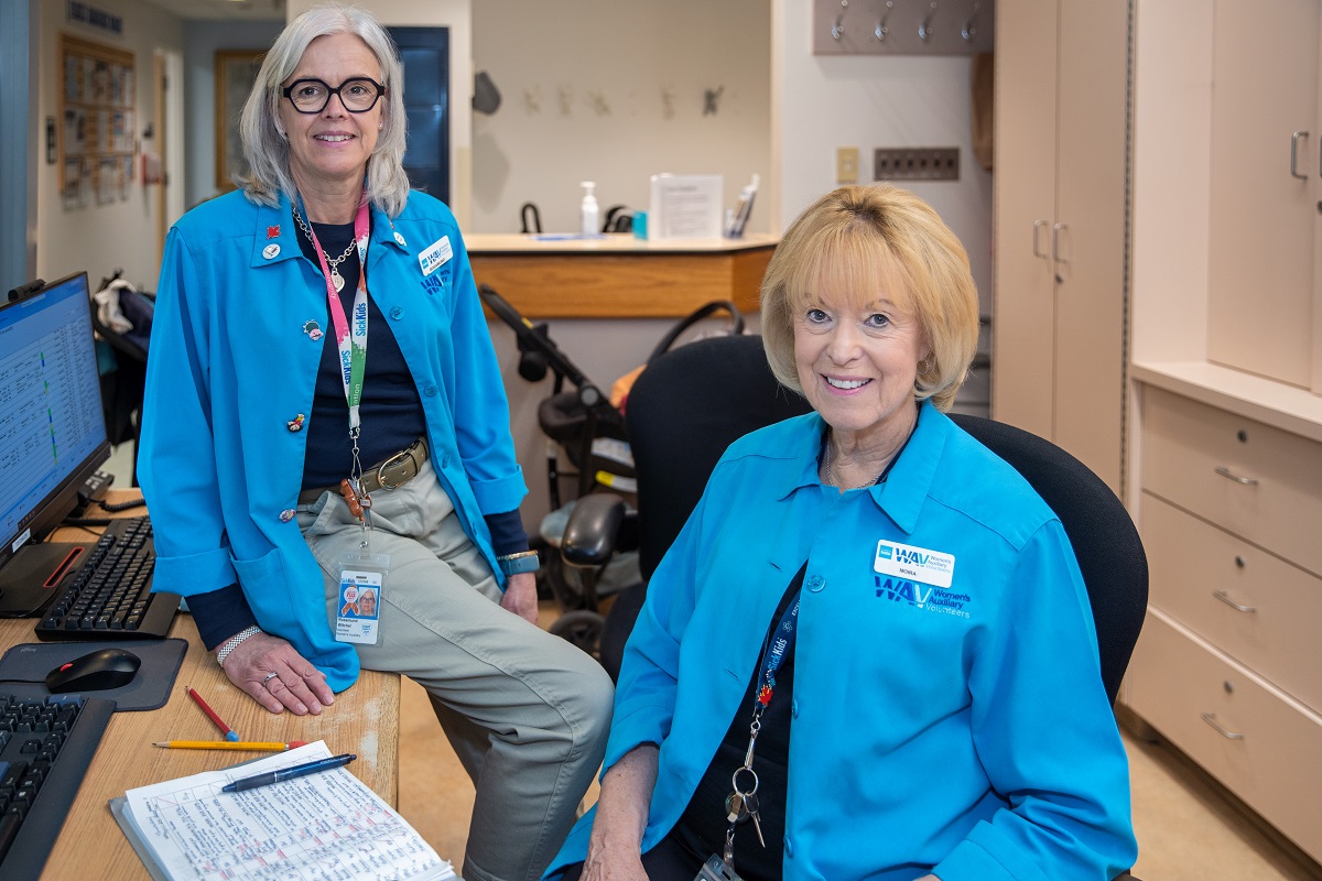 Two women in blue jackets seated near a desk.