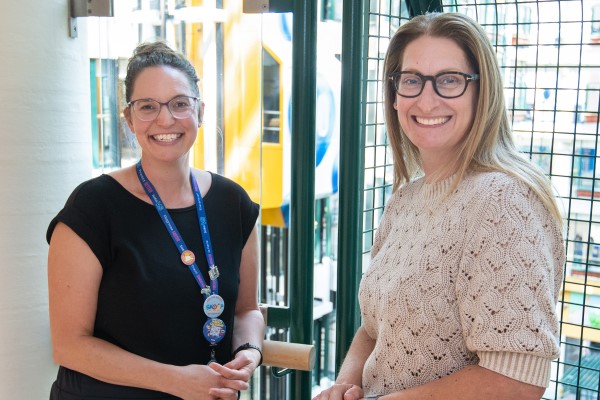 Katie and Shaindy smile with the Atrium elevators visible behind them. 